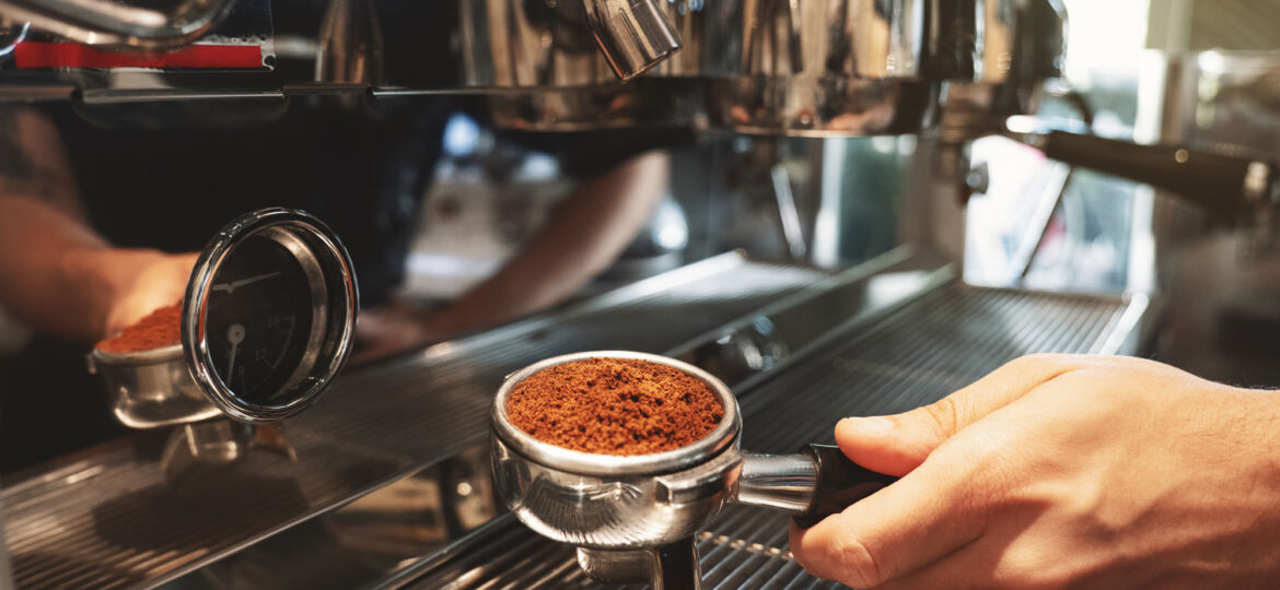 barista holding coffee holder with ground coffee near professional coffee machine close up