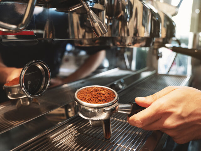 barista holding coffee holder with ground coffee near professional coffee machine close up